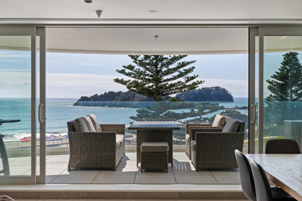 un patio con sillas y mesas y vistas al océano en Oceanside Bliss - Absolute Beachfront - Uninterrupted Ocean Views with Pool, en Mount Maunganui