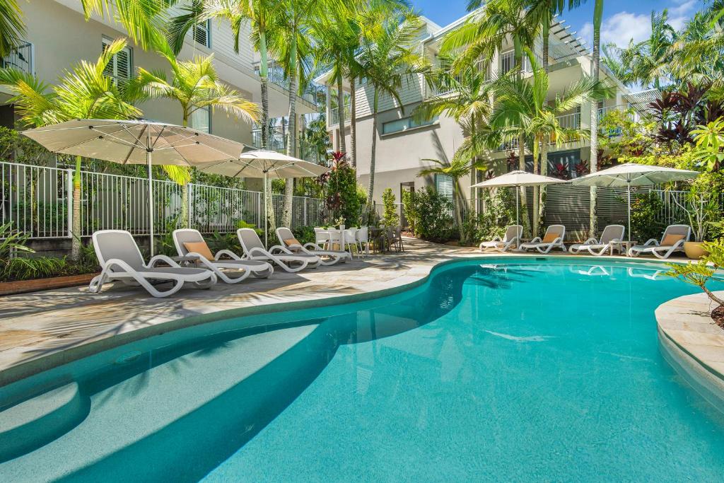 a swimming pool with chairs and umbrellas next to a building at Metzo Noosa Resort in Noosaville