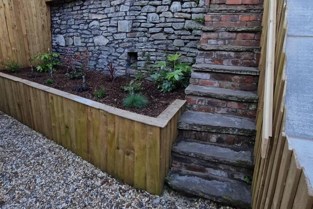 a garden with a stone wall and a wooden fence at Modern 4-Bedroom Townhouse With Private Garden in Abertillery