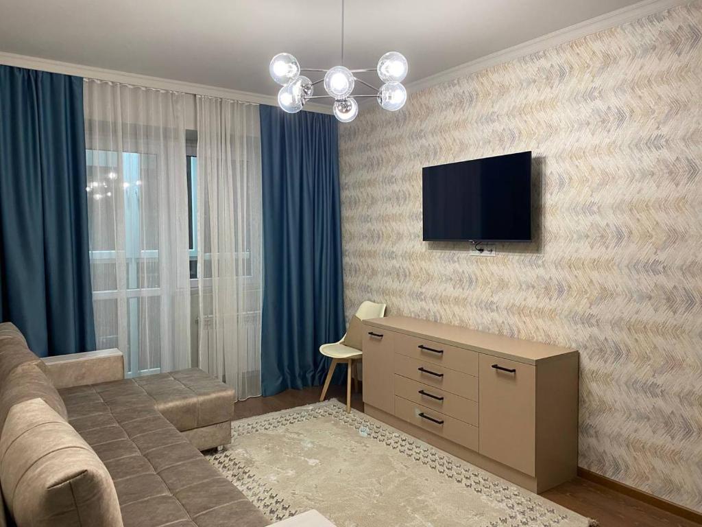 uma sala de estar com um sofá e uma televisão na parede em Уютная квартира-студия ЖК Теремки em Almaty