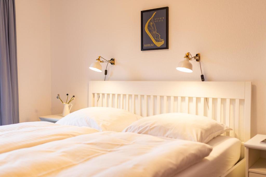 1 dormitorio con 2 almohadas blancas y 2 lámparas en Haus am Seezeichen - Whg. Lürßen, en Wittdün