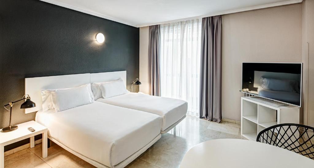 - une chambre avec un grand lit blanc et une télévision dans l'établissement Sercotel Togumar, à Madrid