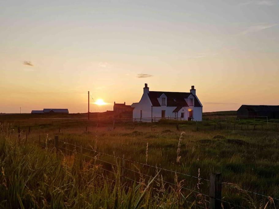 a house in a field with the sunset in the background at Traditional Croft house in Creagorry
