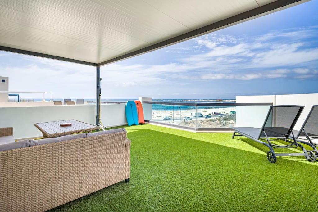 a balcony with green grass and a couch and an umbrella at Casa Corralito - 2 bed apartment with sea and sunset views in Cotillo