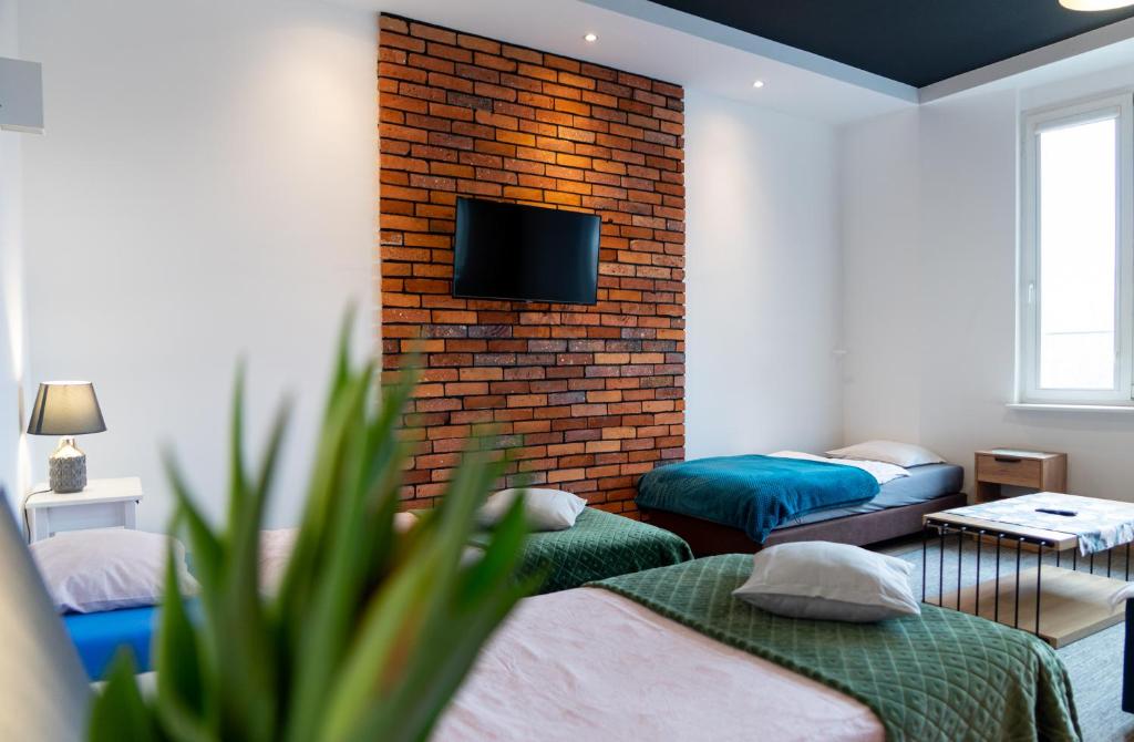 a room with two beds and a tv on a brick wall at Apartamenty Weneckie in Zielona Góra