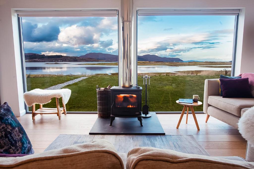 a living room with a fireplace in front of a large window at The Shorehouse in Broadford