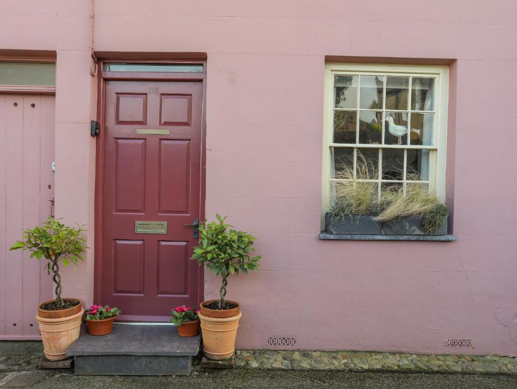 ein rosafarbenes Haus mit einer roten Tür und Topfpflanzen in der Unterkunft Seagull Cottage in Beaumaris
