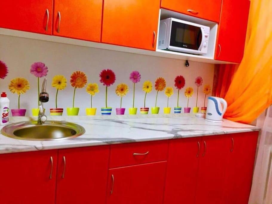 eine Küche mit roten Schränken und einem Waschbecken mit Blumen an der Wand in der Unterkunft Уютная однушка на 7м in Temirtaū
