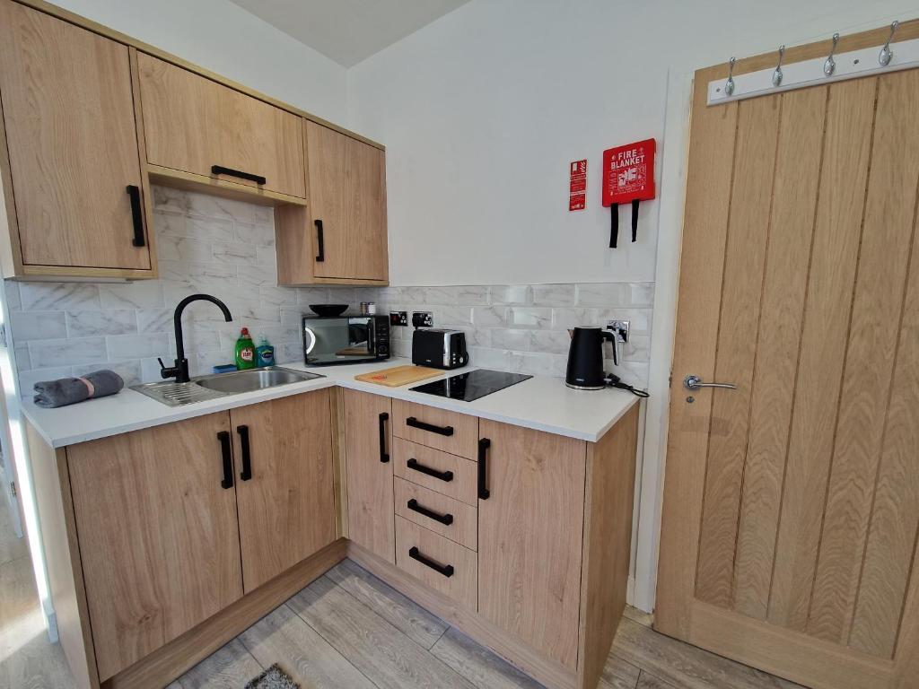 a small kitchen with wooden cabinets and a sink at Flat 1, Modern studio apartment, Tynte Hotel, Mountain Ash in Quakers Yard