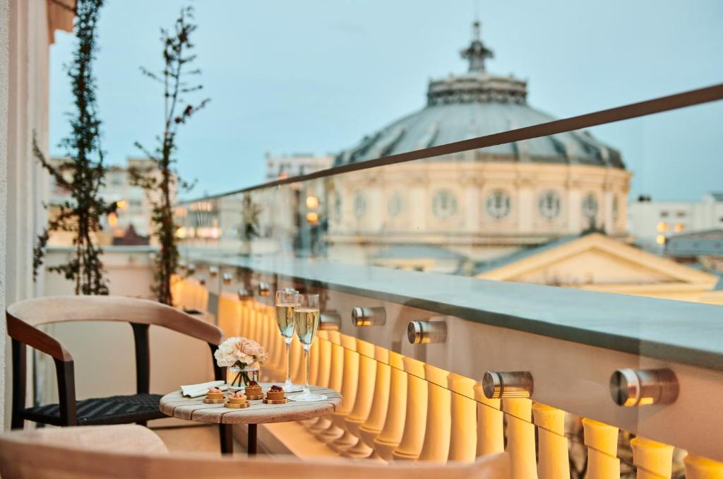 Rooftop balcony with glass railing, two glasses of champagne, small pastries and flowers, domed city view at dusk at InterContinental Athenee Palace Bucharest by IHG in Bucharest
