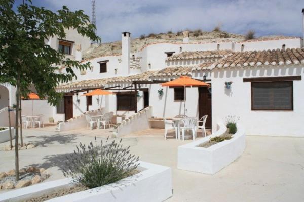 un patio con mesas y sombrillas frente a un edificio en Cuevas Cañada Honda, 
