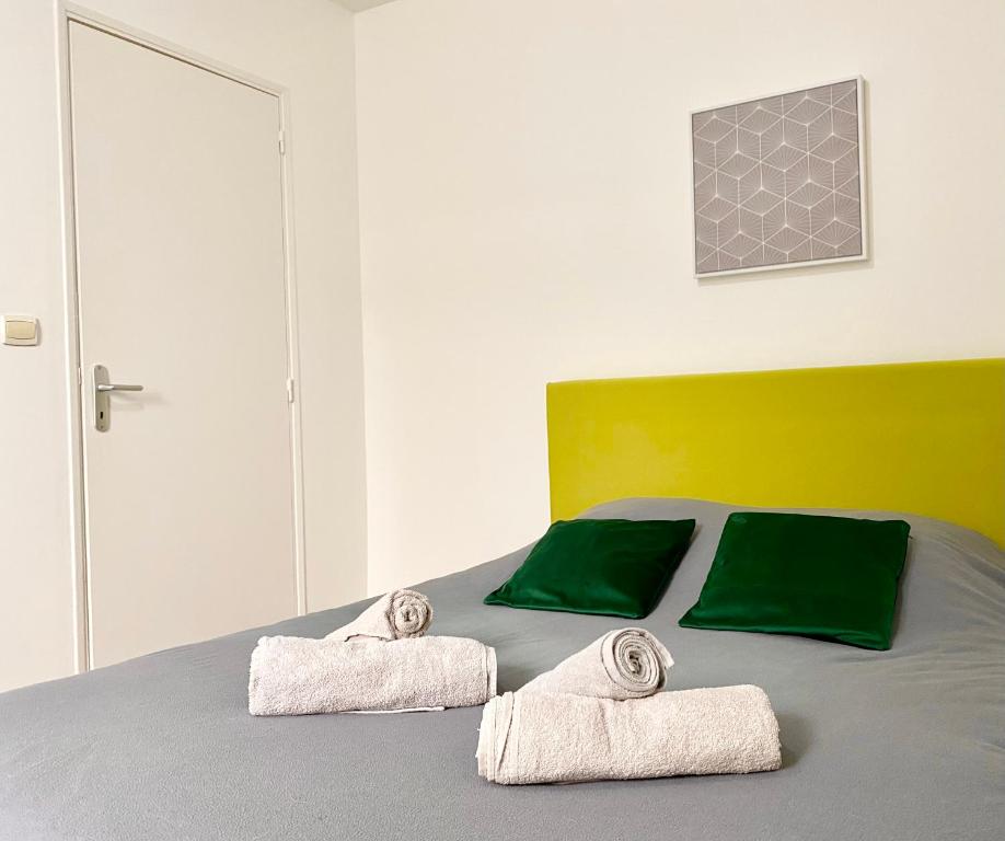 een slaapkamer met een bed met groene kussens en handdoeken bij * Le Droma D’or * Appartement Confort * Centre-ville in Calais