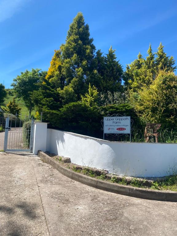 a white fence with a sign in front of trees at Upper Grippath Farm Holiday Cottages in Newport