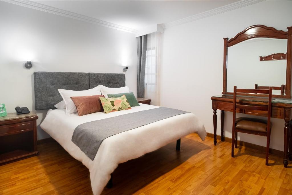 a bedroom with a bed and a desk and a mirror at Hotel Virrey Central in Bogotá