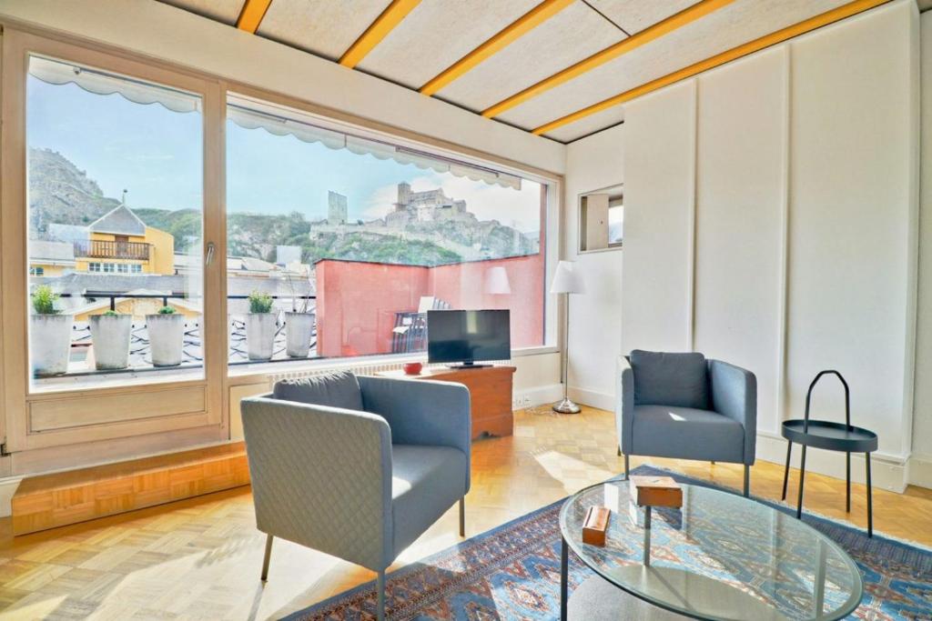 uma sala de estar com duas cadeiras e uma televisão e uma grande janela em Duplex de charme au cœur de la vieille ville de Sion em Sião