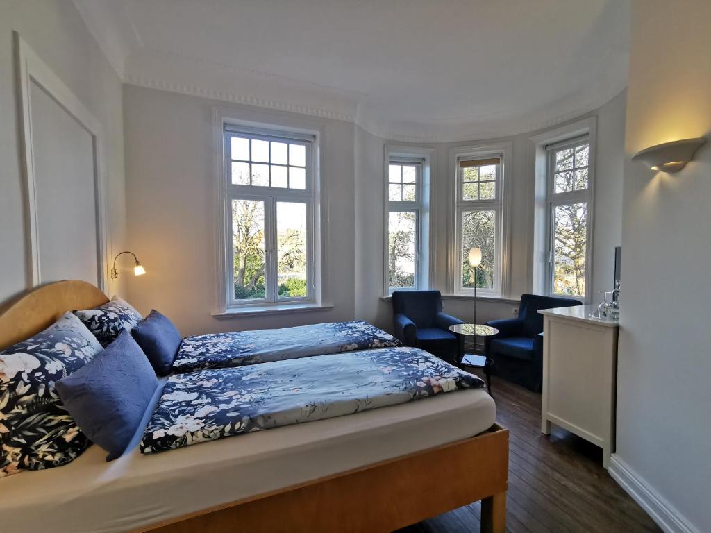a bedroom with a bed and a chair and windows at Villa Deichvoigt in Cuxhaven