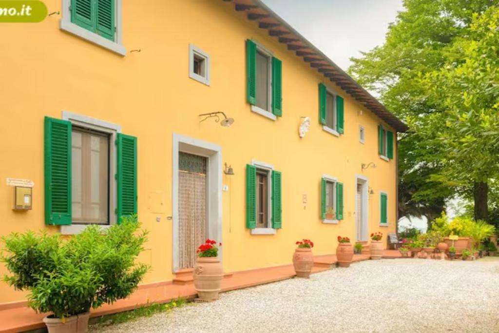 uma casa amarela com persianas verdes e vasos de plantas em Agriturismo La Pineta em Fucecchio