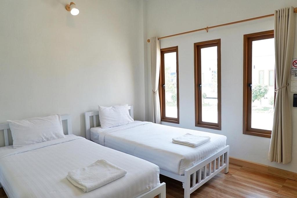 two beds in a room with two windows at Hey Sunday Home in Ban Mit Mongkhon