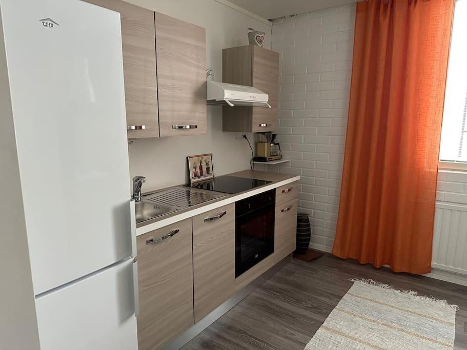una cocina con armarios de madera y una cortina naranja en Huoneisto kaupungissa Ylivieska, en Ylivieska