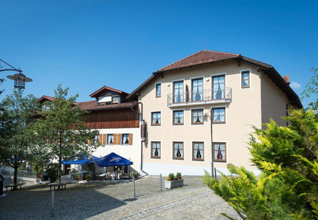 a large tan building with a blue umbrella in front of it at Landhotel Zum Jägerstöckl in Grafenau