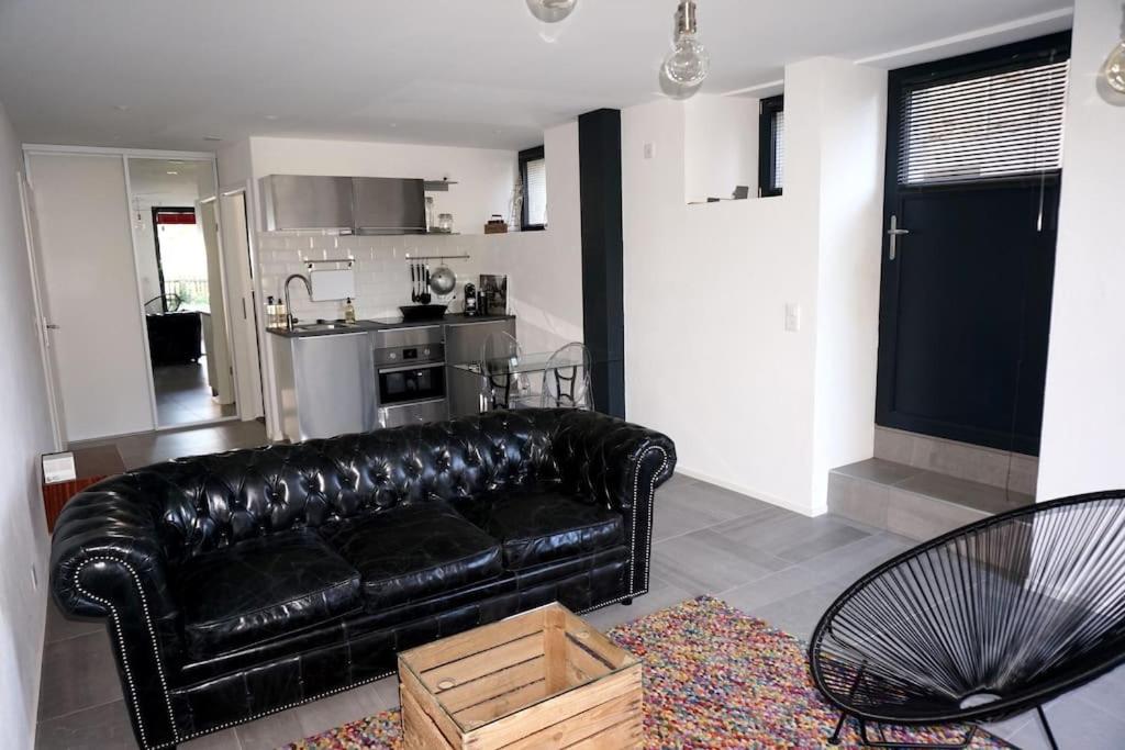 a black leather couch in a living room with a kitchen at Beau studio dans ancienne grange rénovée. in Blonay