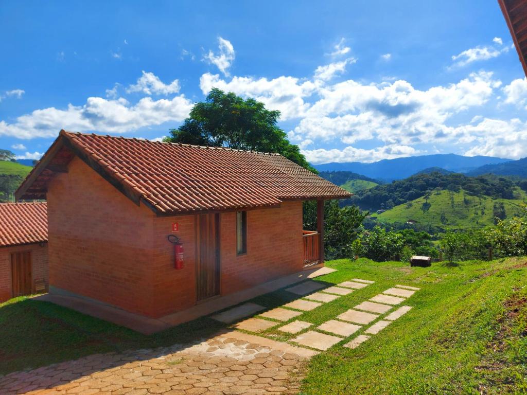 uma pequena casa num campo com montanhas ao fundo em Chalés Santa Luzia em Santo Antônio do Pinhal