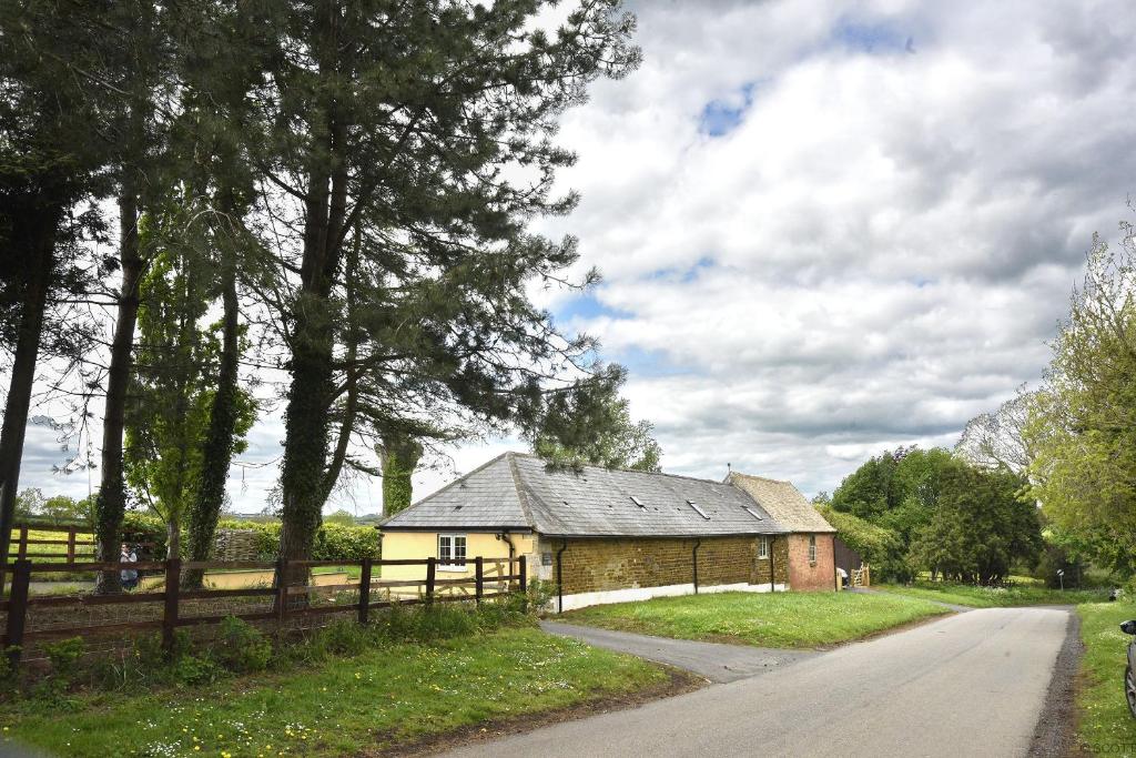 an old building with a fence next to a road at The Old Stables at Castle Chase, Ayston in Uppingham