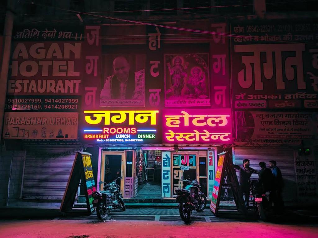 deux motocycles garés devant un bâtiment avec panneaux de néons dans l'établissement Jagan Hotel & Restaurant, à Dhaulpur