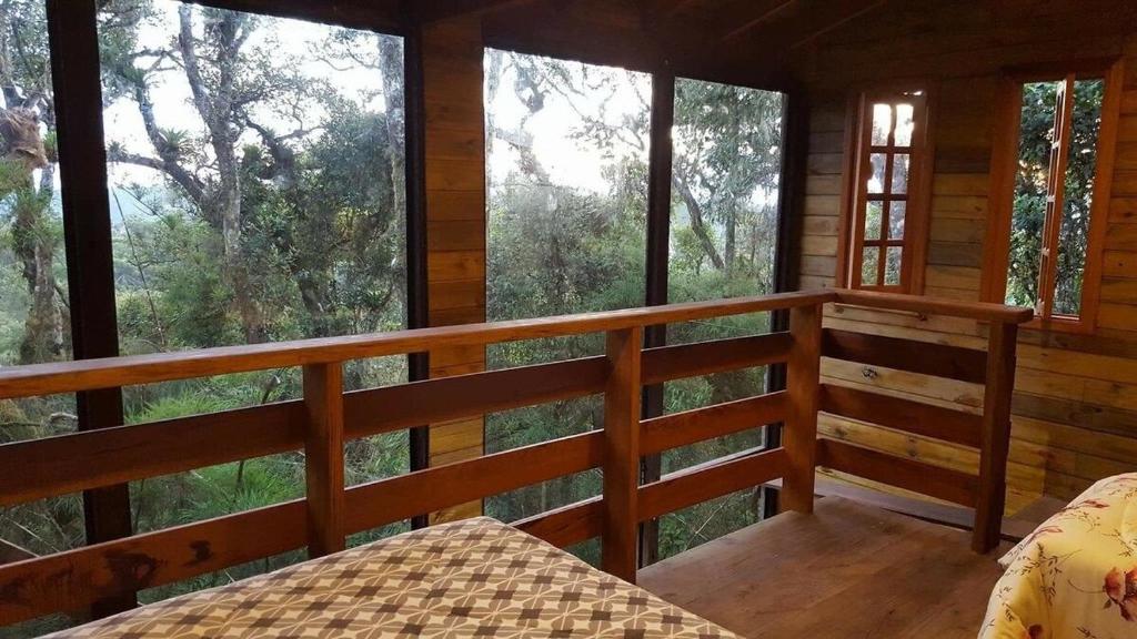 1 dormitorio en una cabaña de madera con vistas al bosque en Chalé dos Tucanos- Parede de vidro com linda vista, en Campos do Jordão