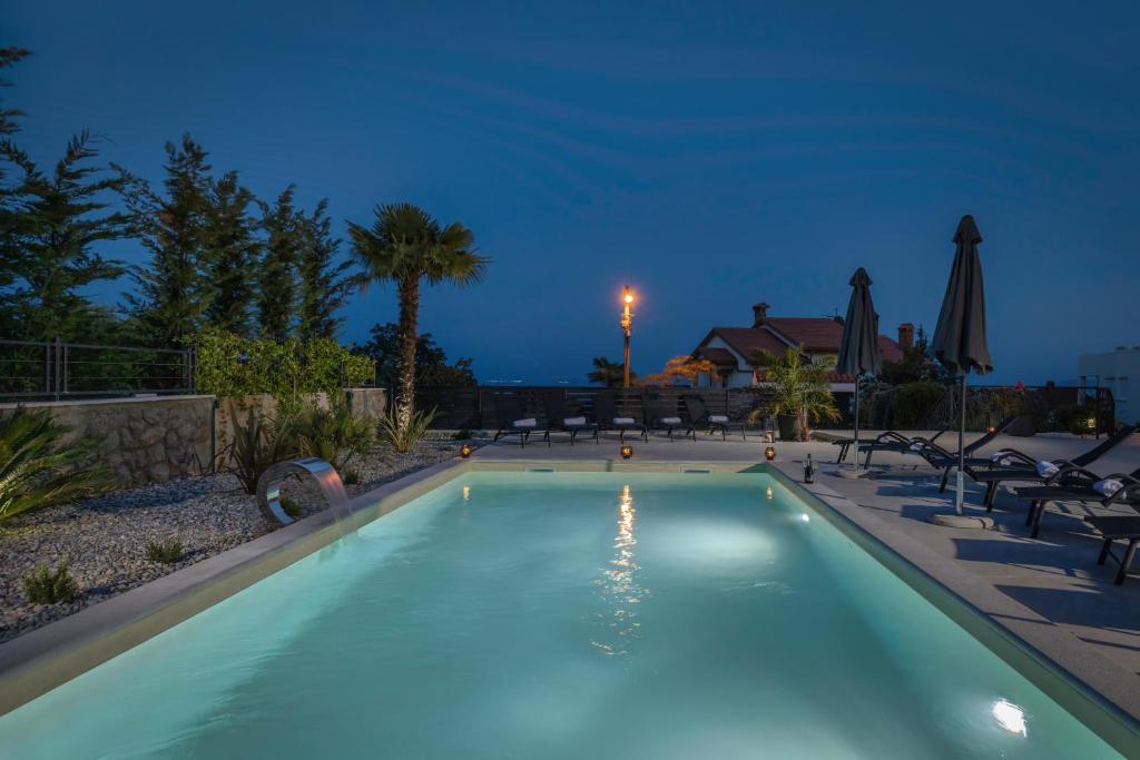 a swimming pool at night with chairs and umbrellas at Piccola Villa Adriatic, with heated swimming pool, Opatija in Ičići