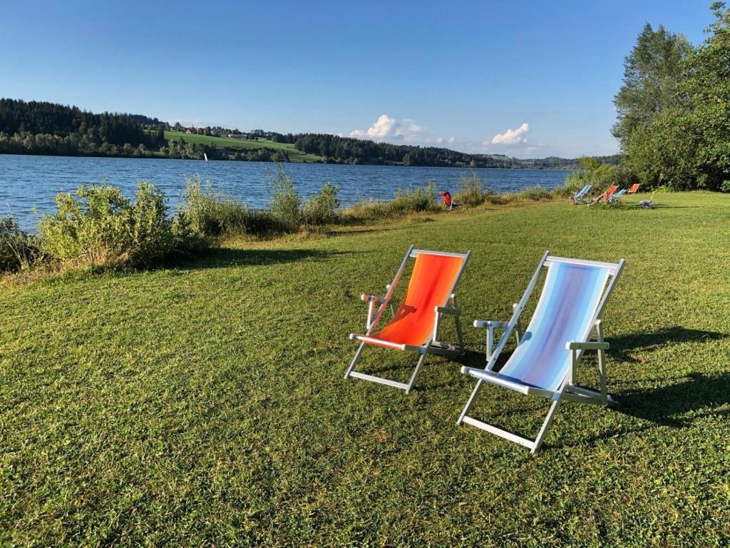 two lawn chairs sitting on the grass next to a lake at Seeglück in Oy-Mittelberg