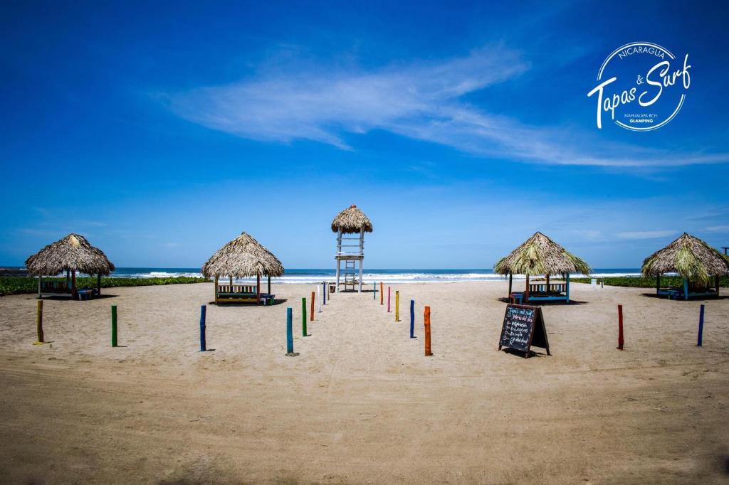 una playa con sombrillas de paja y carteles en la arena en Tapas & Surf, en Petacaltepe