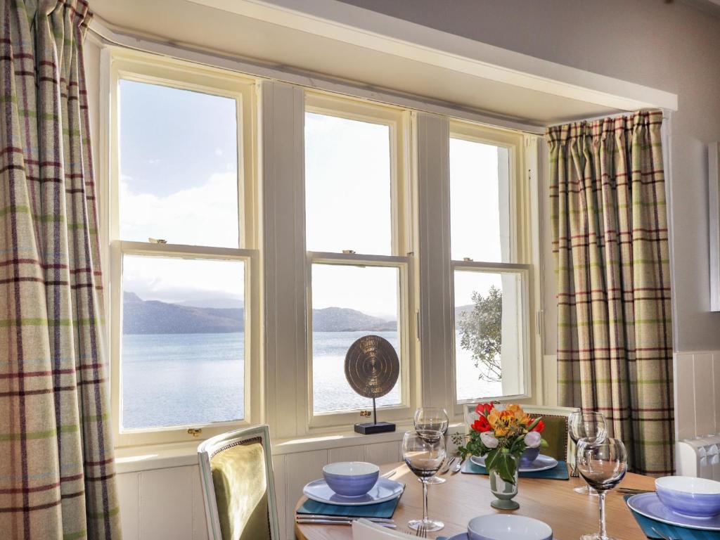 a dining room with a table and three windows at Ferry Cottage - Balmacara in Coillemore