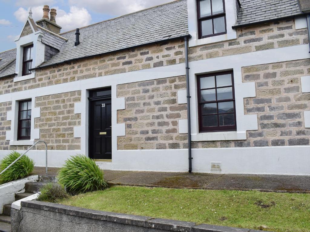 uma casa de tijolos com uma porta preta em Acarsaid Cottage em Portknockie