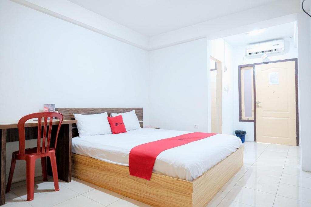 a bedroom with a bed and a red chair at RedDoorz near Tugu Pers Jambi in Jambi
