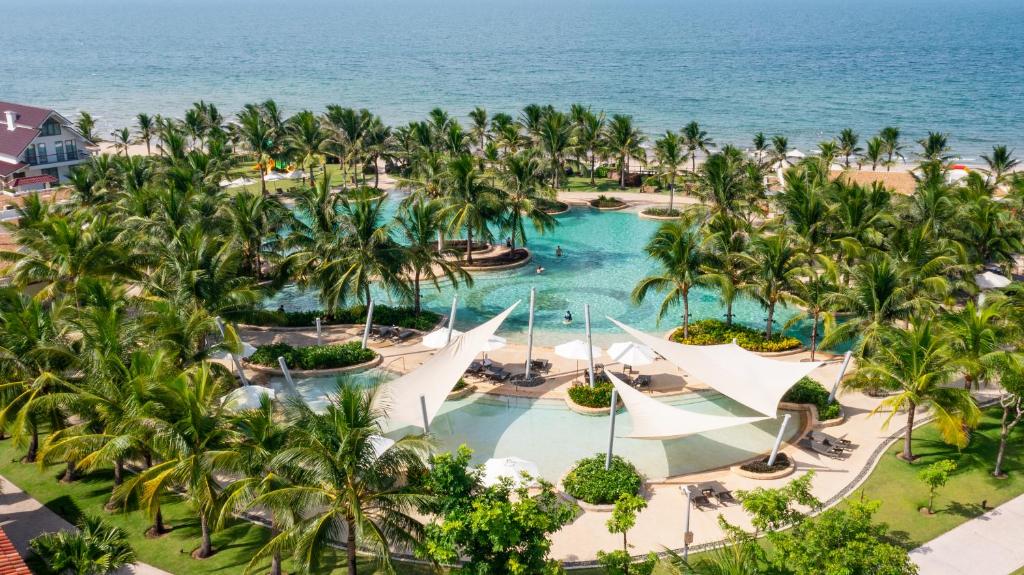 een luchtzicht op een zwembad van het resort met palmbomen en de oceaan bij Citadines Pearl Hoi An in Hội An