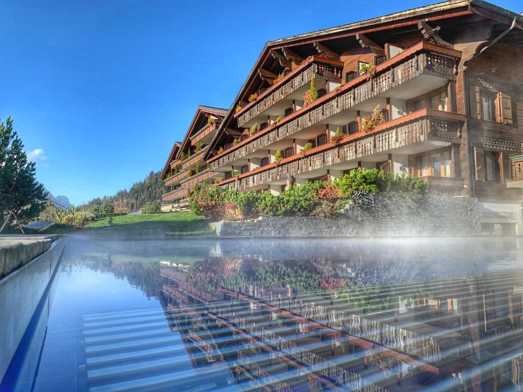 un bâtiment avec une réflexion dans l'eau dans l'établissement ERMITAGE Wellness- & Spa-Hotel, à Gstaad