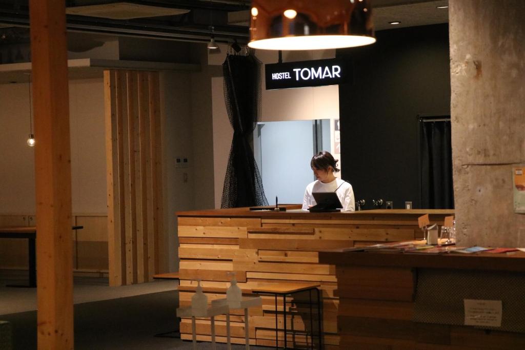 een vrouw zit aan een bureau in een kamer bij Hostel Tomar in Furano