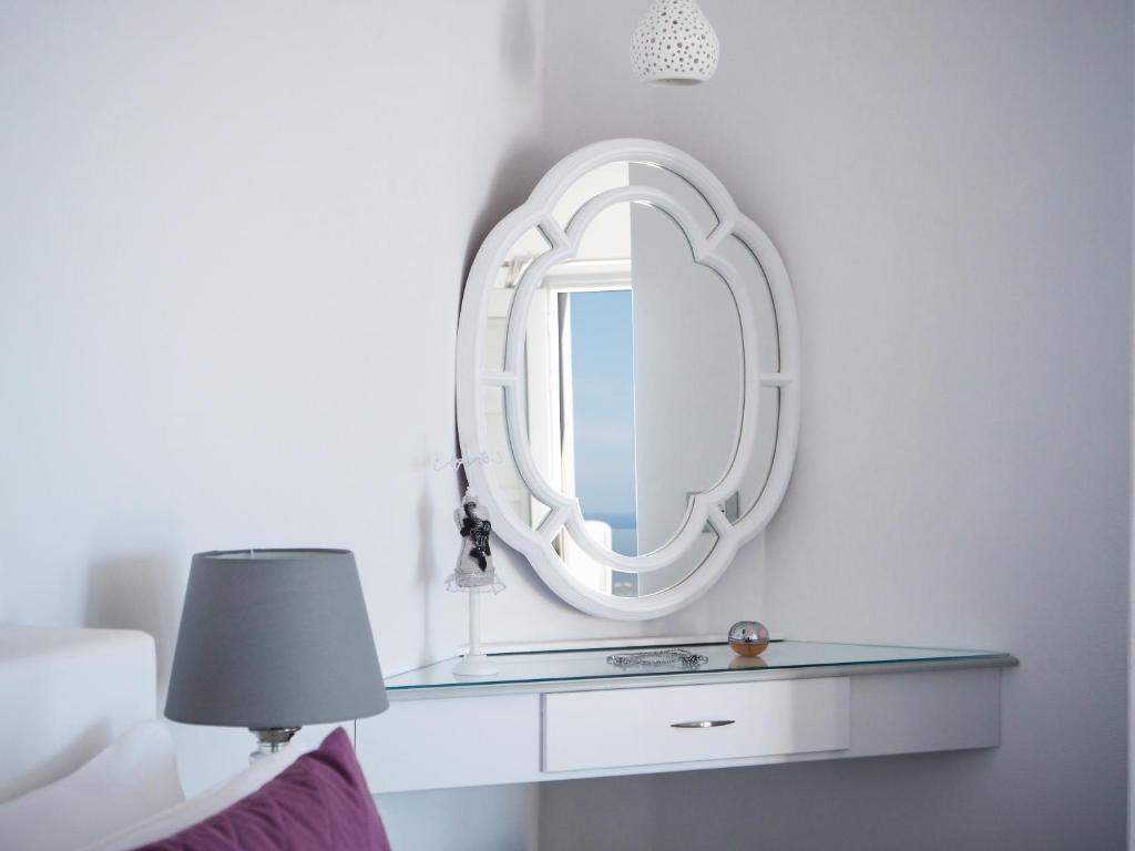 a mirror on a wall above a table with a lamp at Vitsentzos Suites in Imerovigli