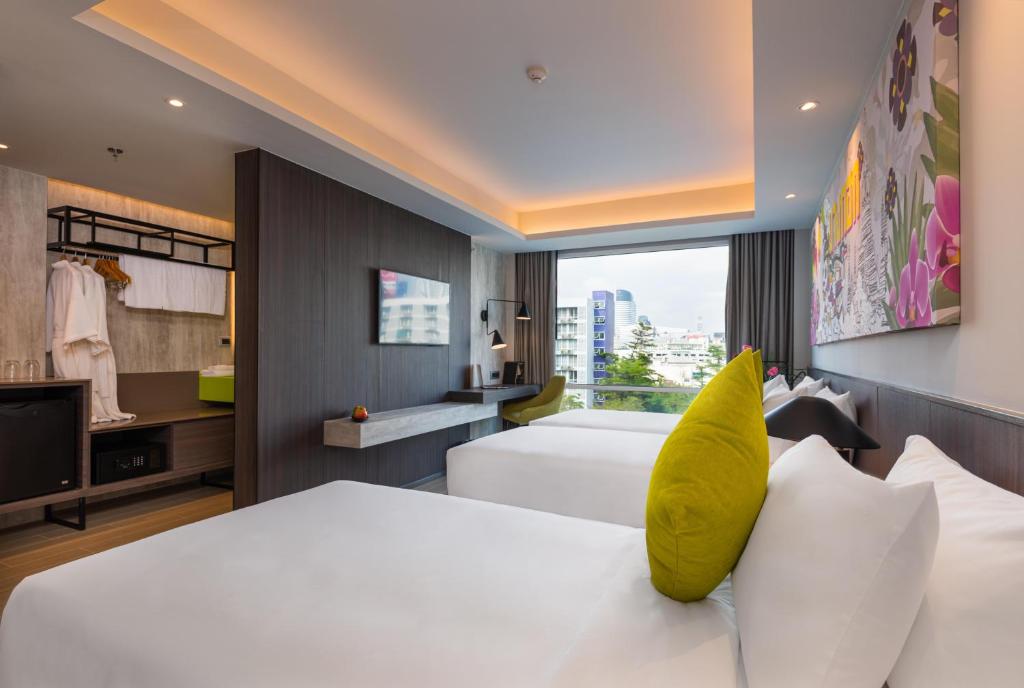 A twin-bed room photographed from the sleeping area toward the desk, television and city window.