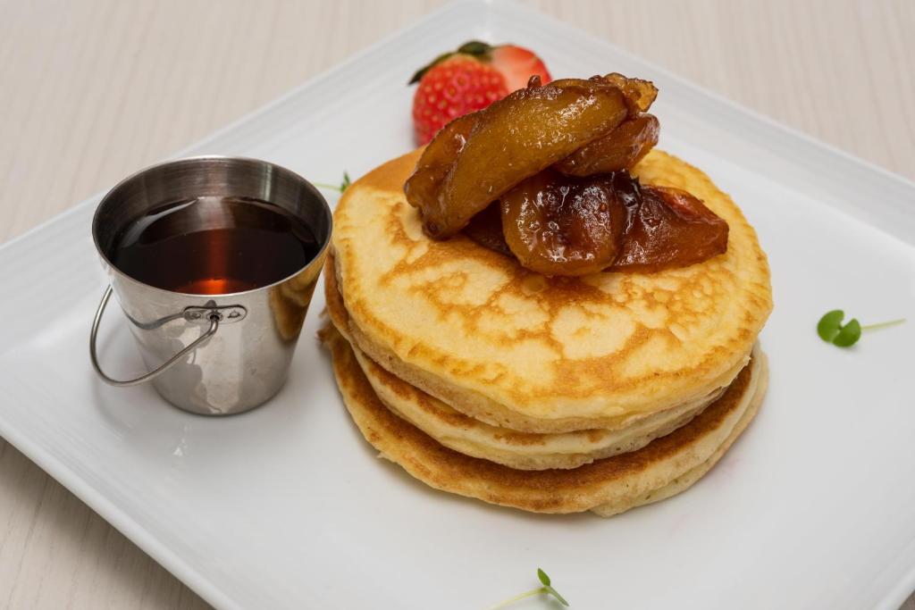 A plated stack of pancakes topped with caramelized fruit and served with syrup.