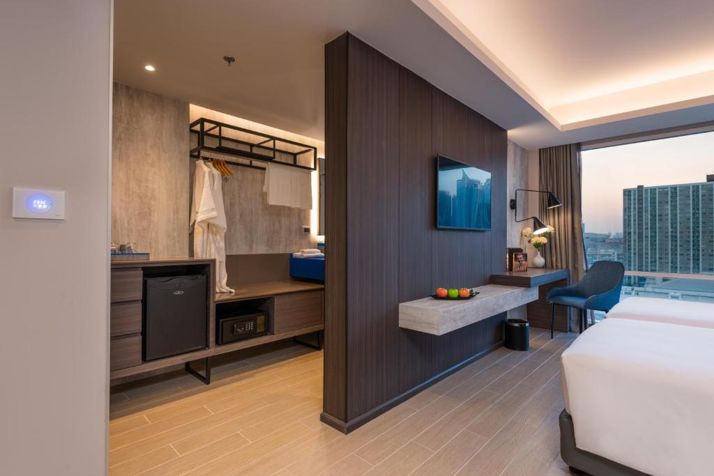 A room view showing the bed edge, work area, television, wardrobe and city-facing window.