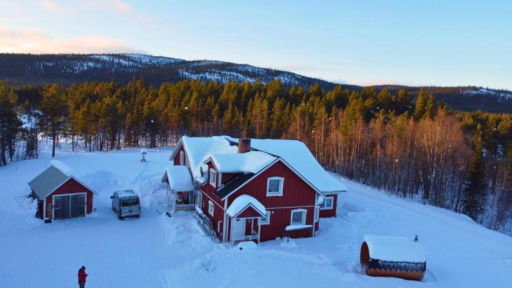 ein rotes Haus im Schnee mit einem Auto daneben. in der Unterkunft Villa Björklund in Arjeplog