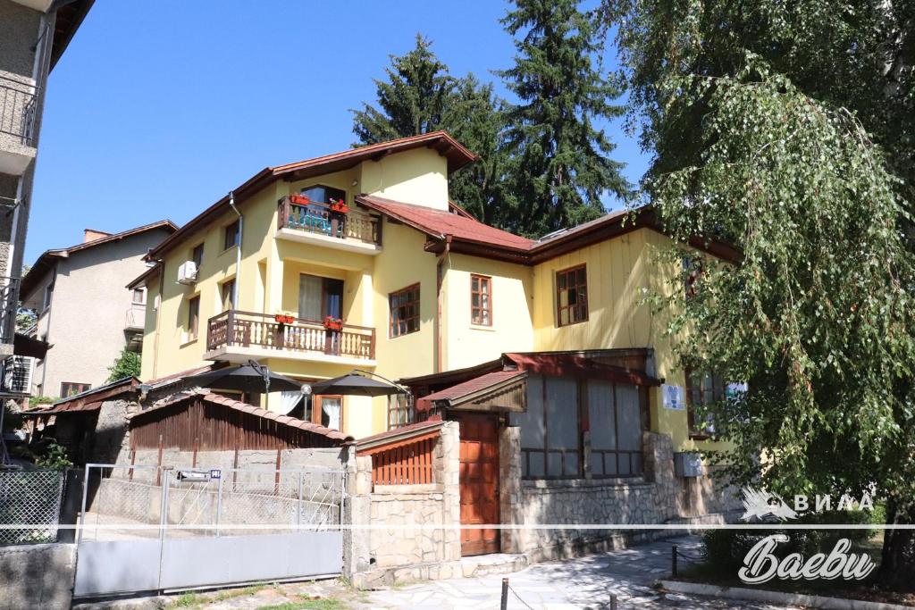 a yellow house with a balcony on a street at ВИЛА БАЕВИ in Velingrad