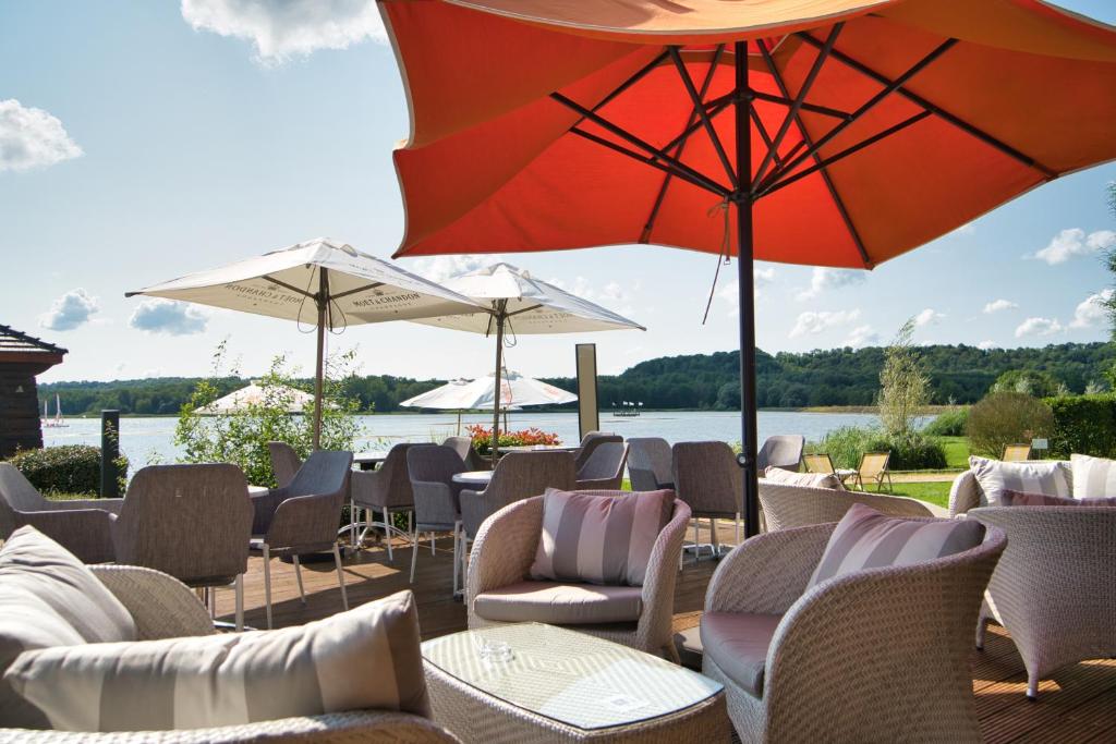 a patio with chairs and umbrellas and a body of water at Hôtel du Golf de l'Ailette, The Originals Relais (Qualys-Hotel) in Chamouille