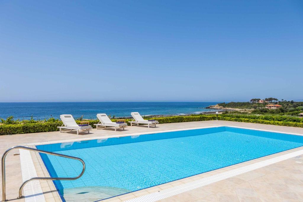 una piscina con sillas y el océano en el fondo en Villa Alba Minies, en Minia