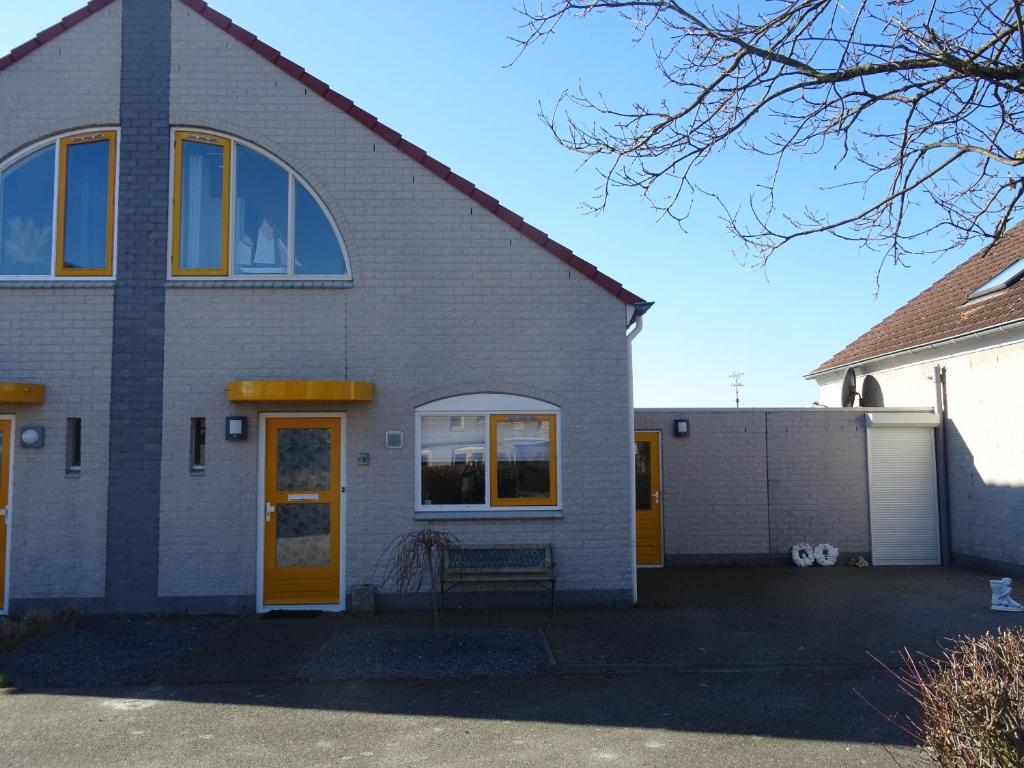 a gray house with a yellow door and a fence at Kustverhuur, Vakantiepark Fort Soleil 23 in Breskens