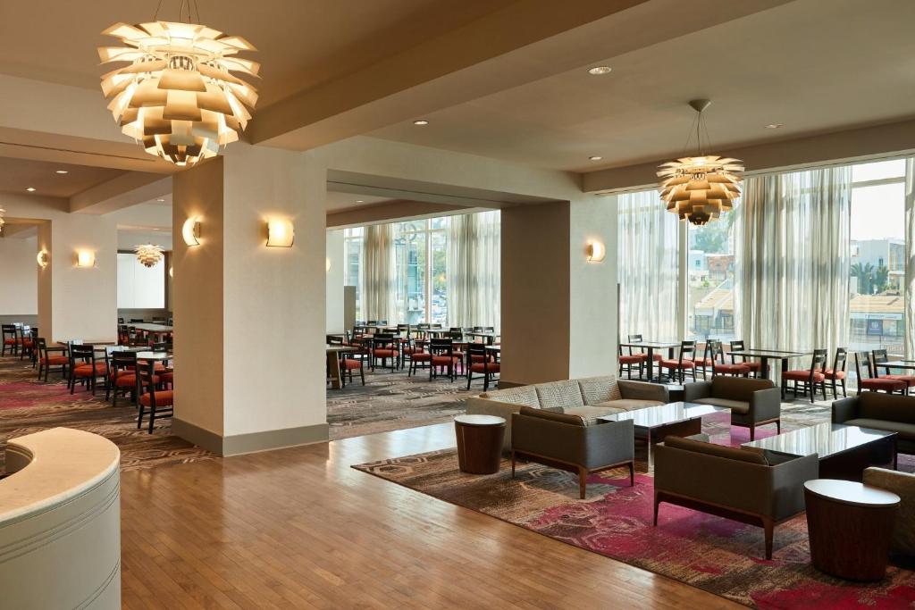 un restaurante con mesas, sillas y ventanas grandes en Loews Hollywood Hotel, en Los Ángeles