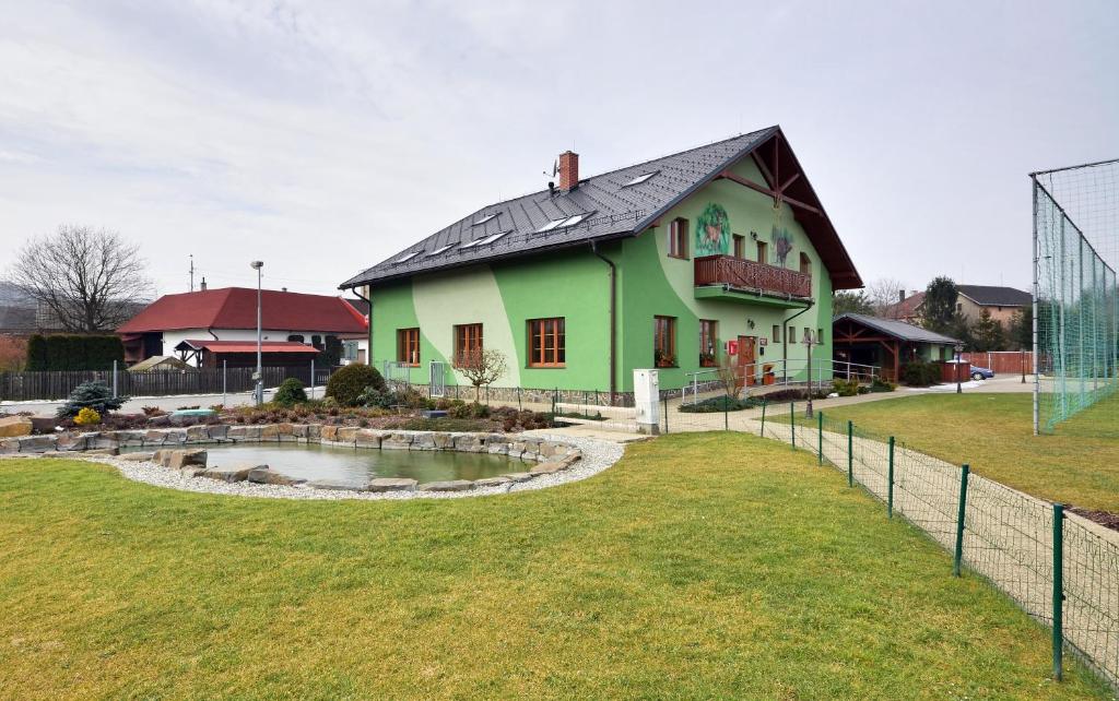 a green house with a pond in front of a field at Restaurace a penzion Kamenec in Jilešovice