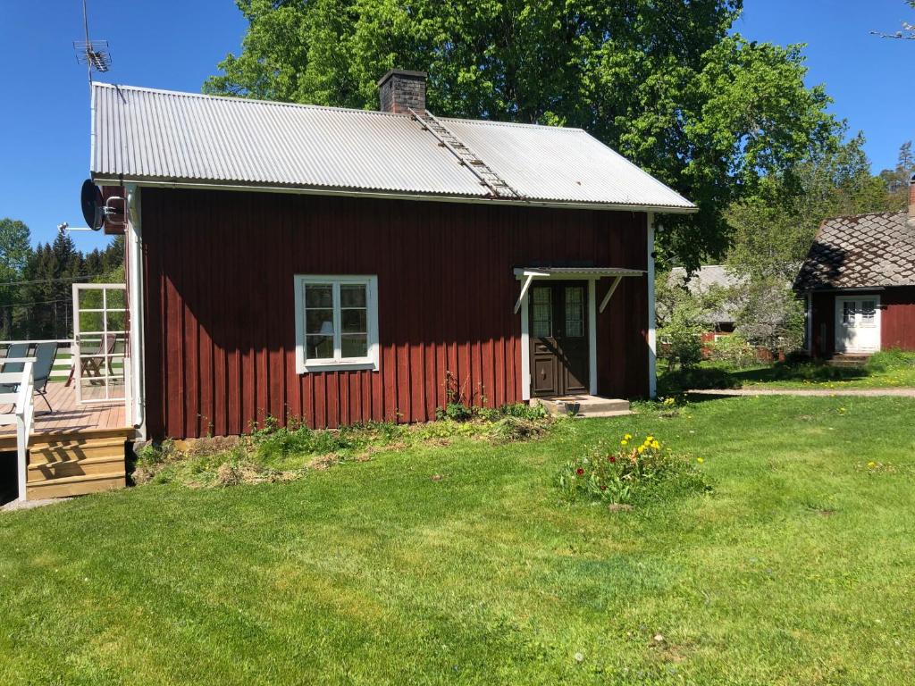 a red barn with a grass yard in front of it at Mysig lantlig stuga, Nycklarör in Korsberga